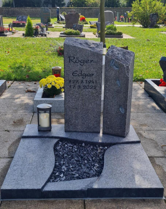 Ein graues Urnengrab auf einem Friedhof mit einem Grabstein bestehend aus zwei einzelnen Steinen.